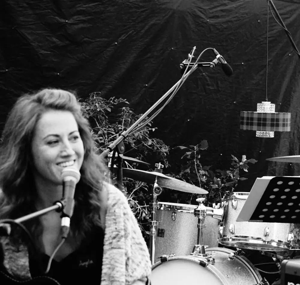 Angie singt lächelnd ins Mikrofon, im Hintergrund ein Schlagzeug